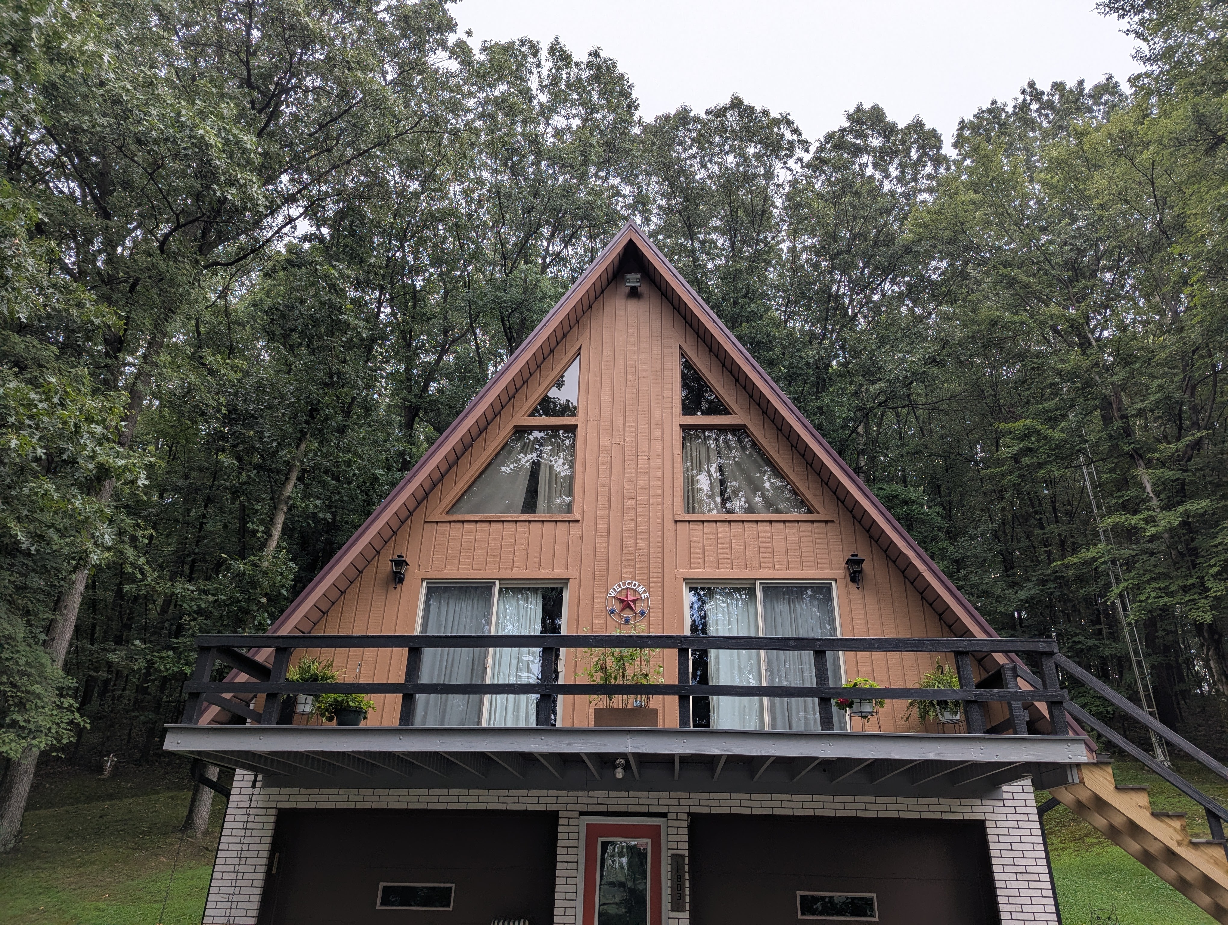 A-frame home with large deck and garage, nestled among green trees.
