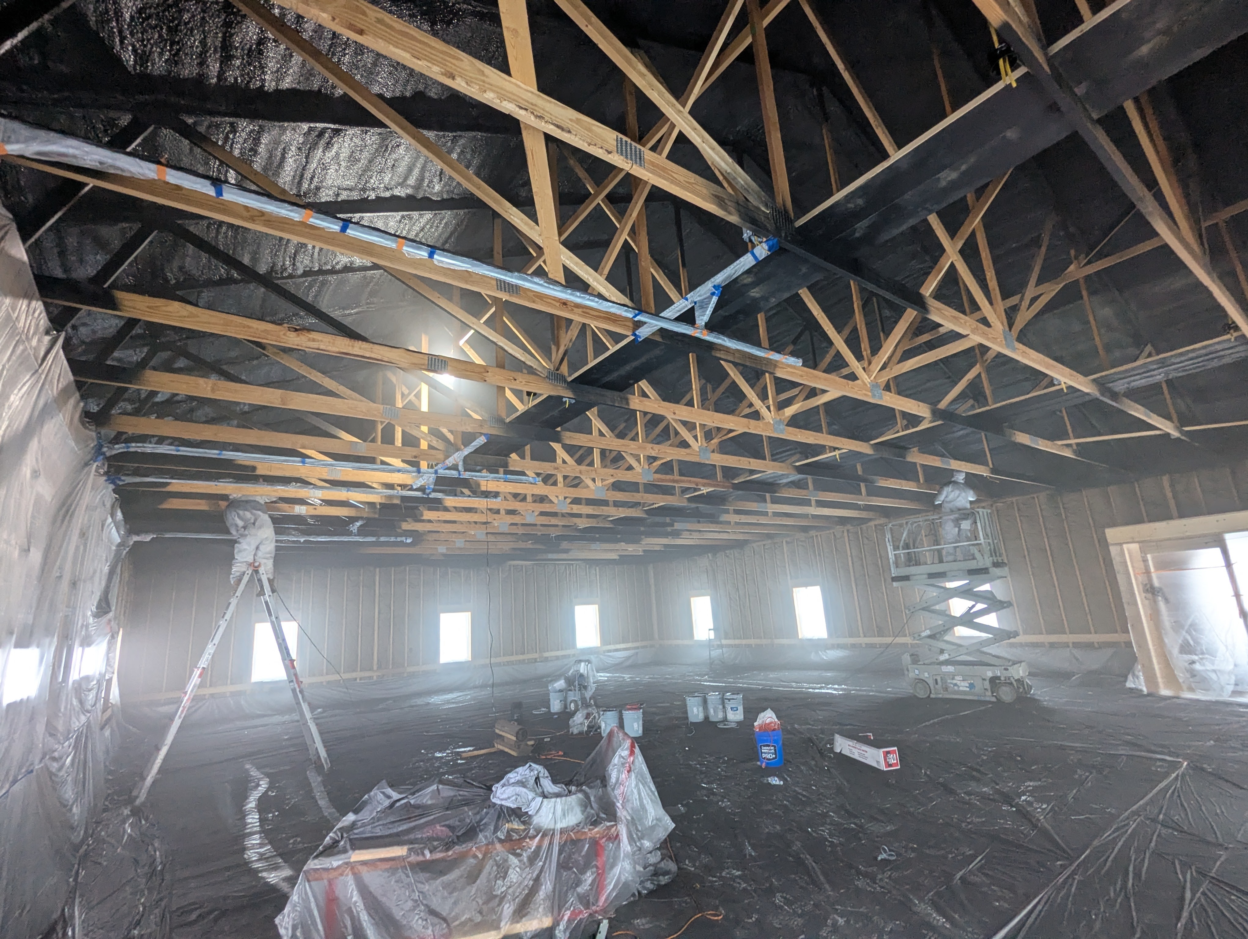 Interior view of a building under construction with exposed wooden beams and painting equipment.