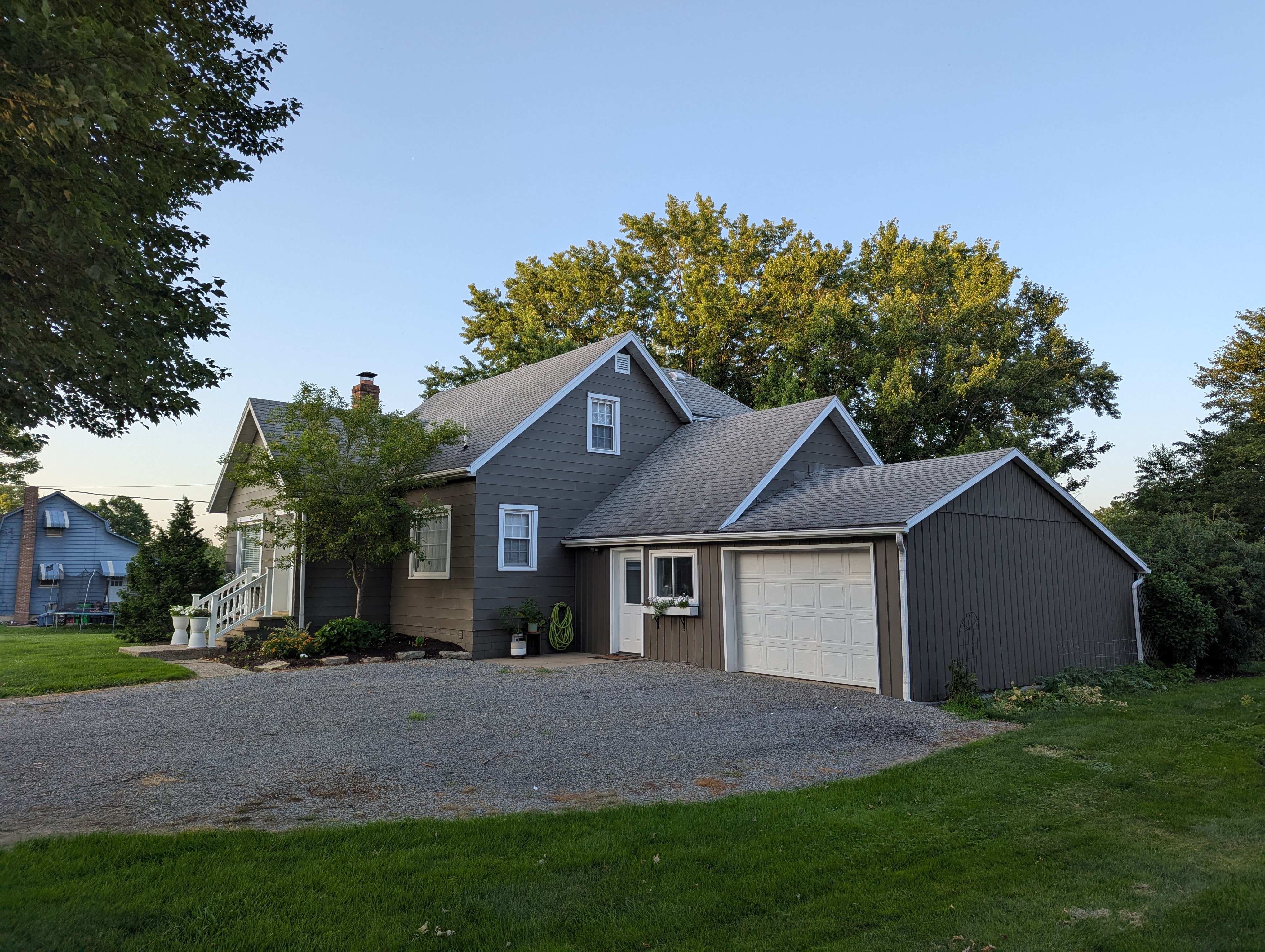 Grey house with white trim, gravel driveway, and green lawn, showcasing our work.