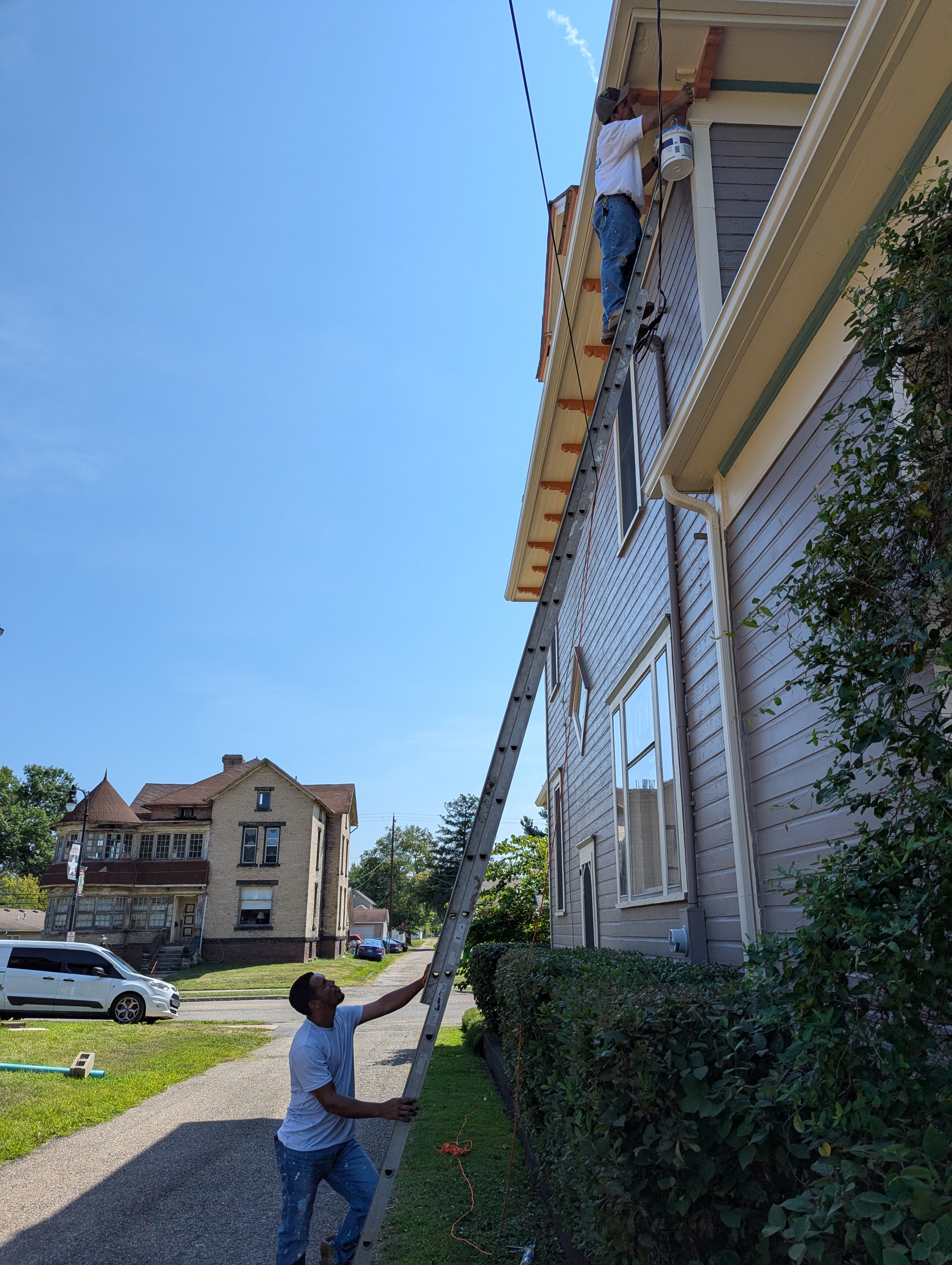 Painters working on exterior house trim with ladder.