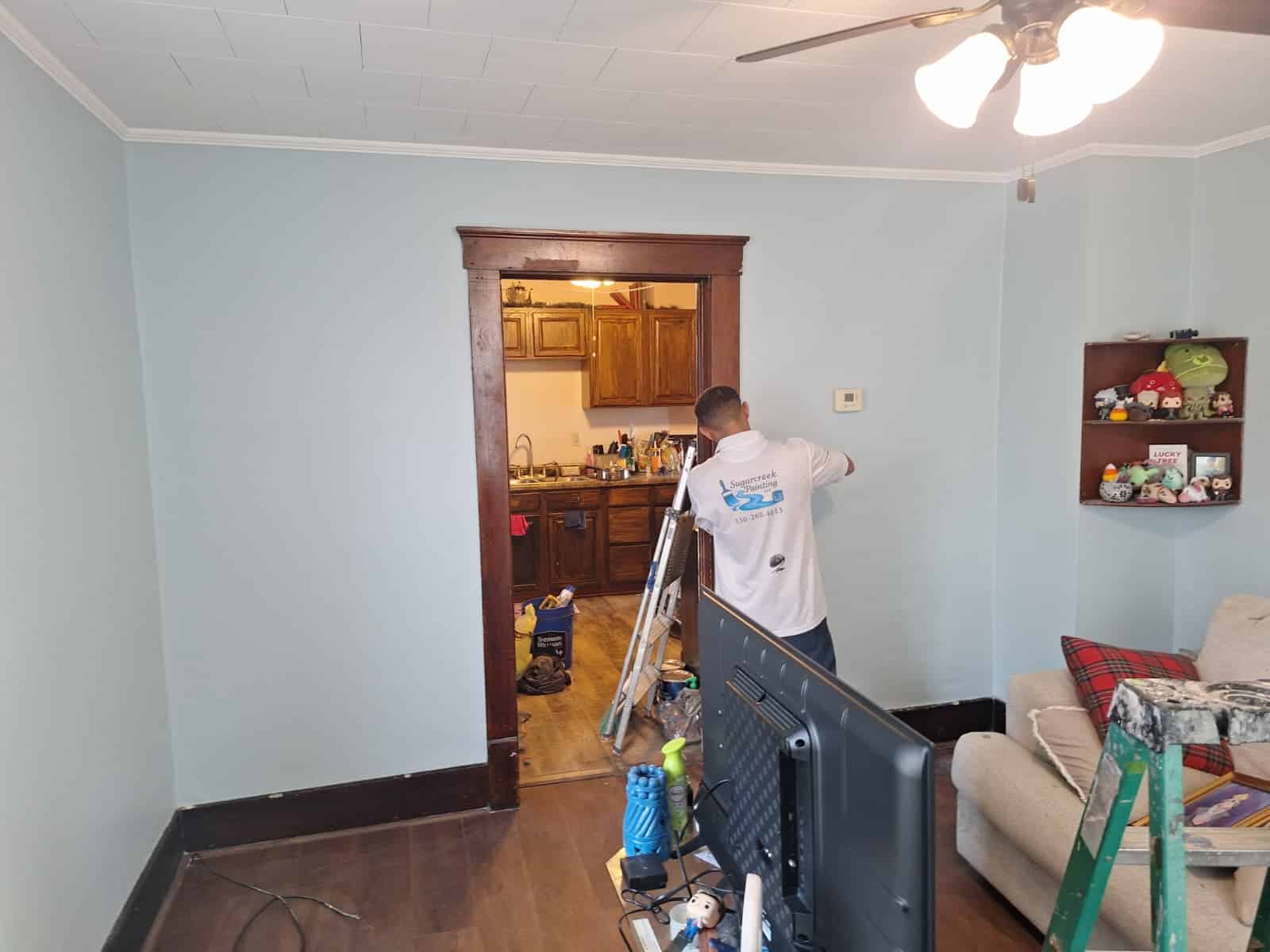 Interior painting project: Worker painting a light blue wall in a home interior.