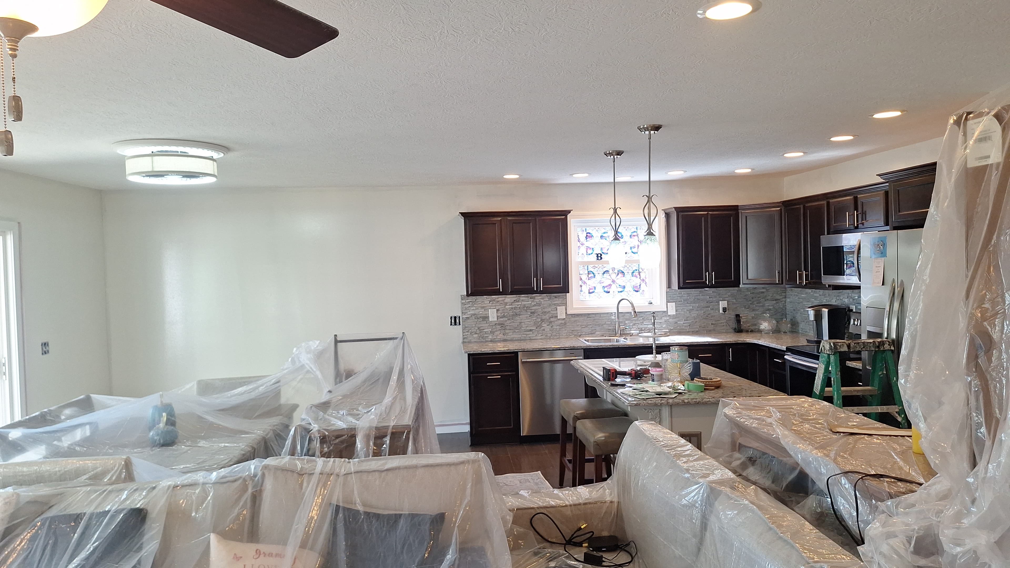 Renovated kitchen and living room with furniture covered in plastic.