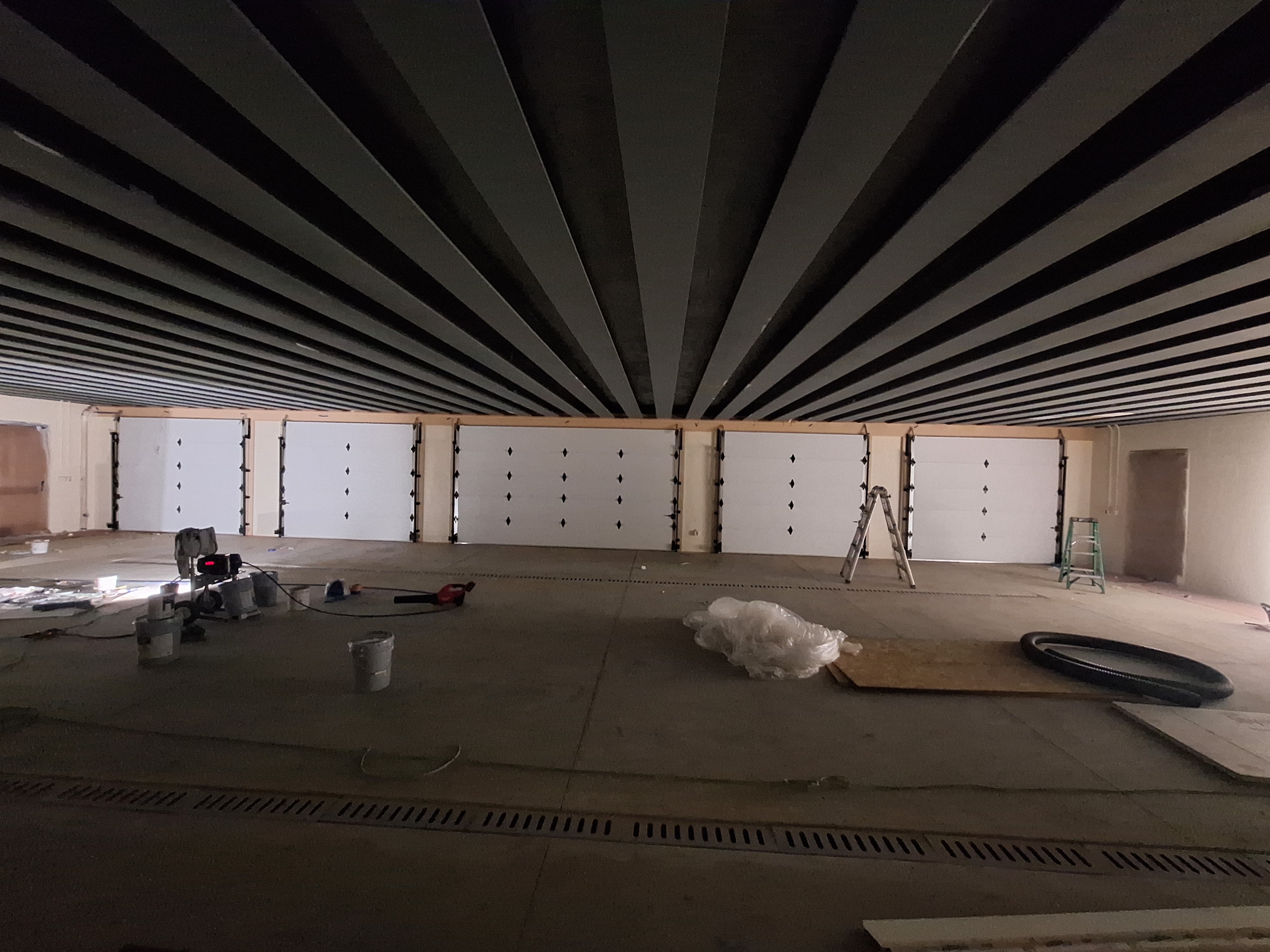 Large garage interior featuring multiple white garage doors and a unique slatted ceiling design.