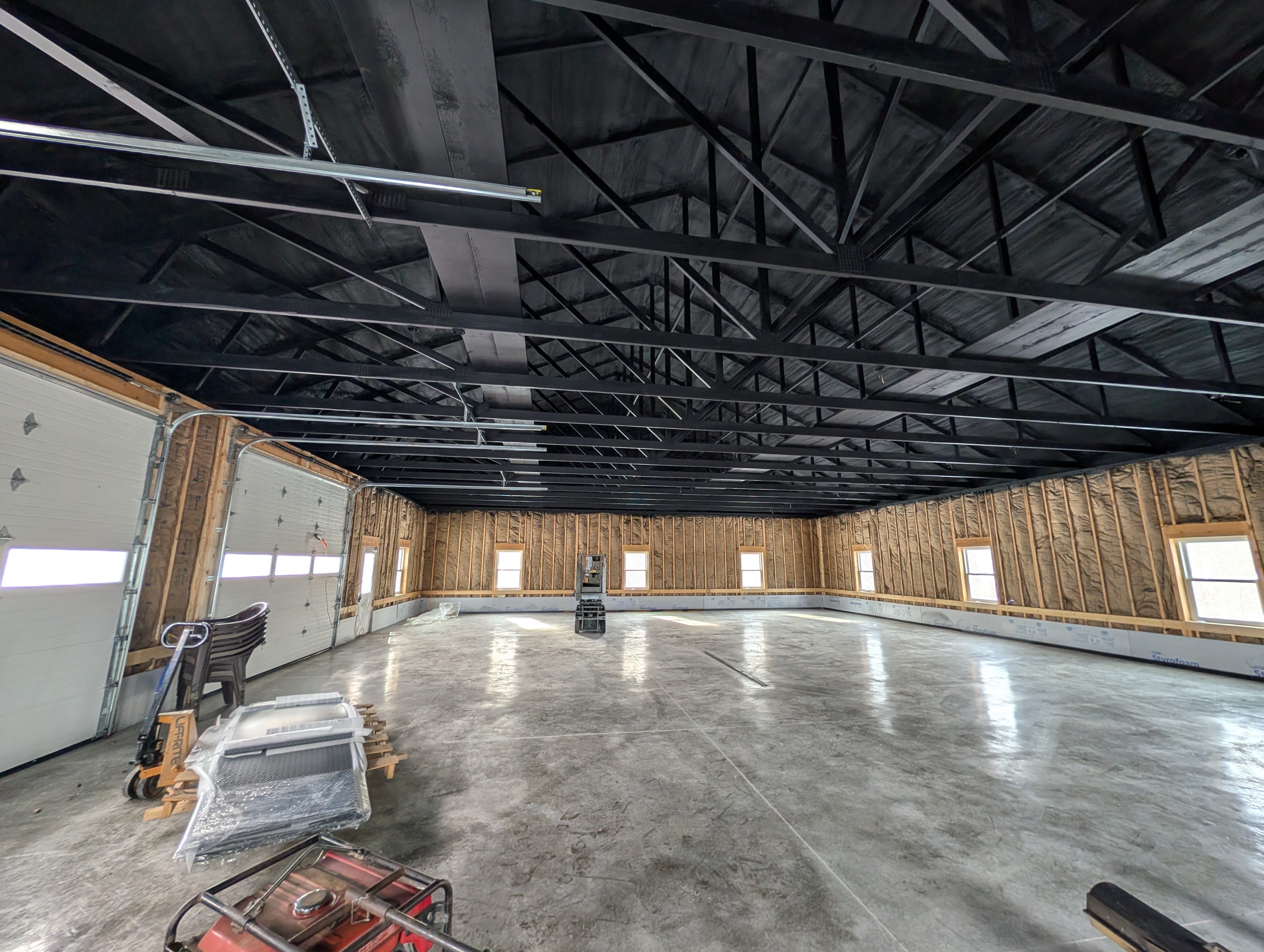 Large garage interior with exposed insulation and painted black ceiling rafters, ready for services.