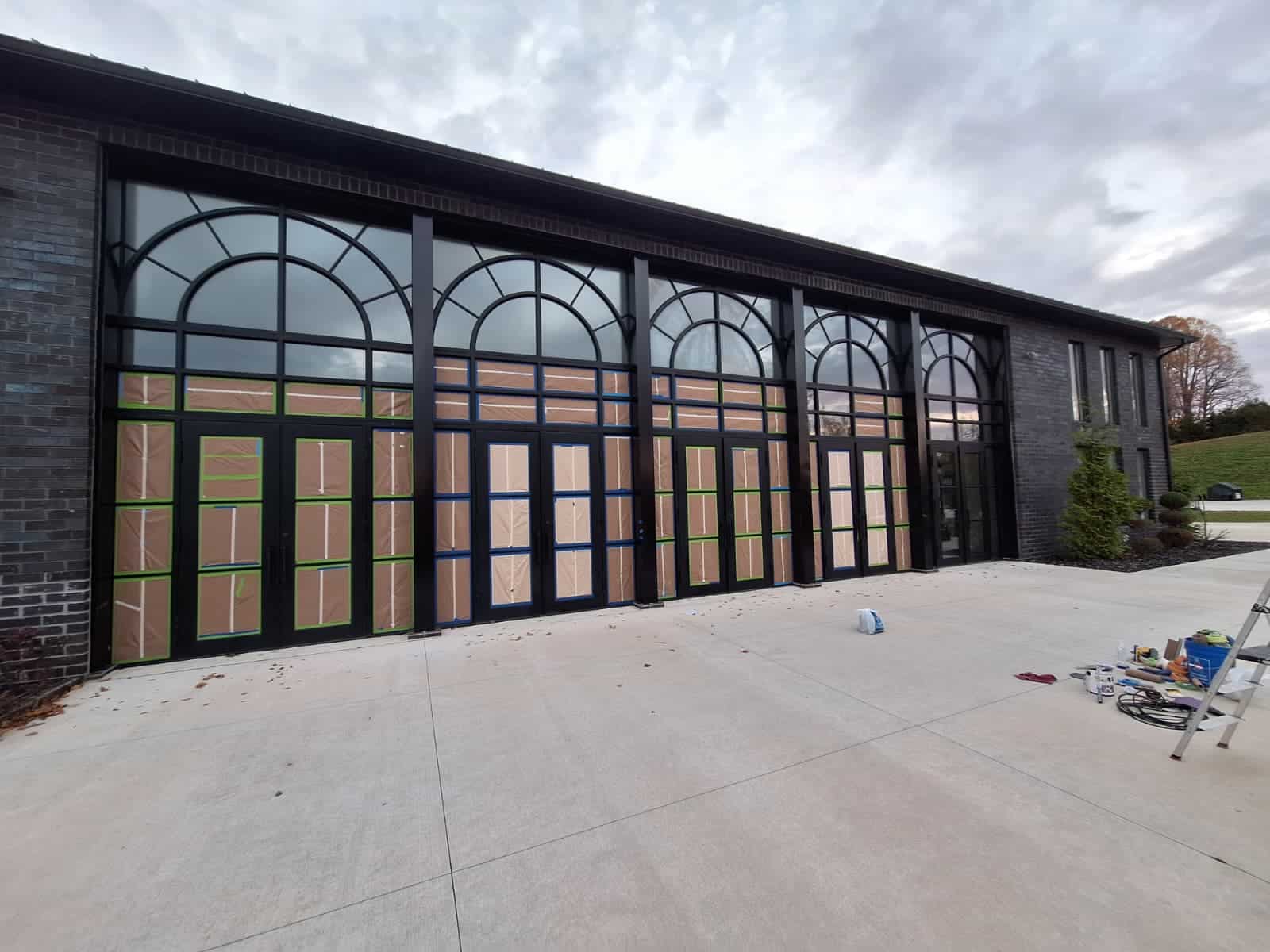Large black arched windows on a brick building, partially covered in protective tape.