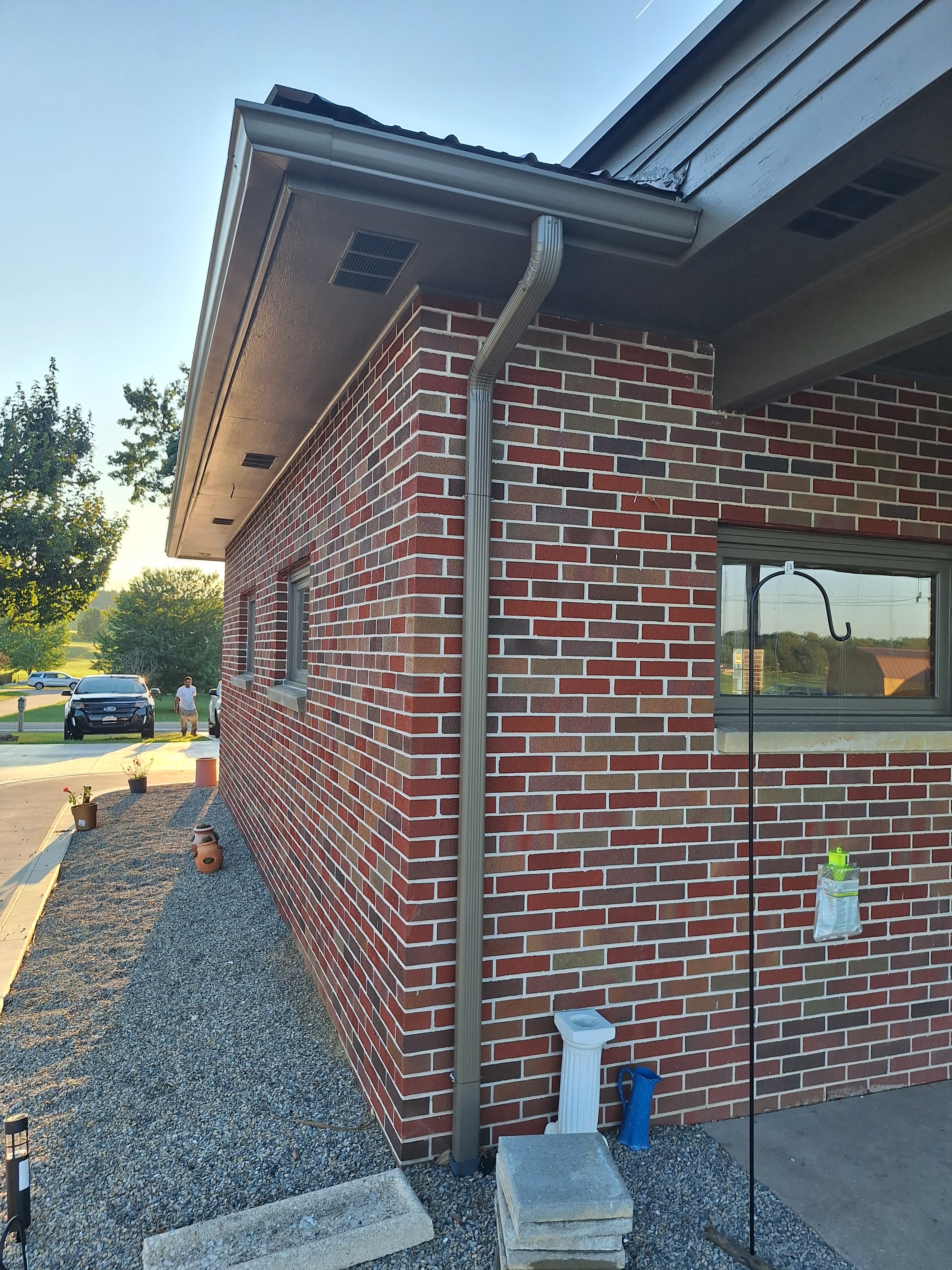 Brick building corner with gray gutters, small windows, and gravel landscaping.