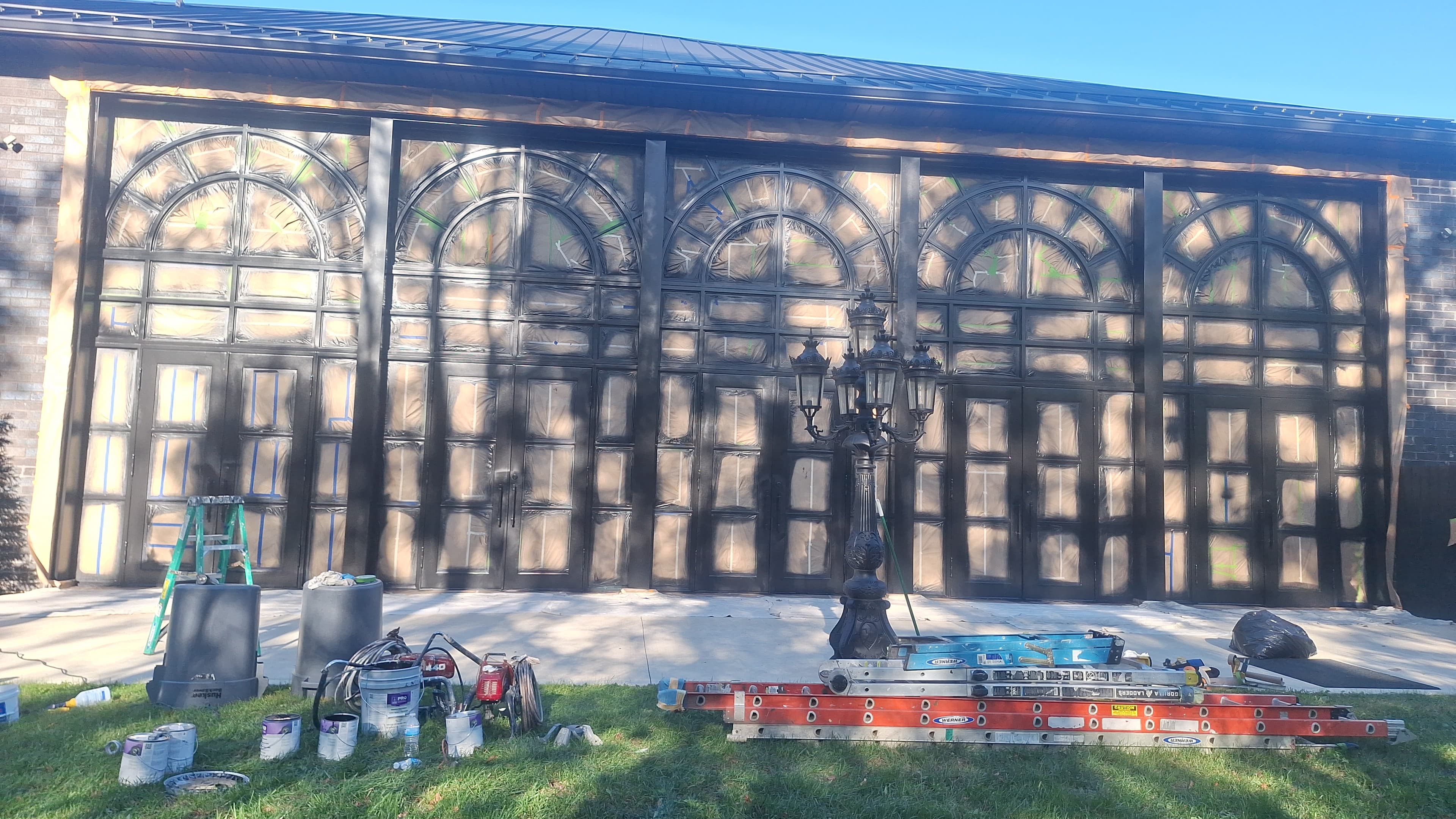 Large garage doors being painted black; ladders and equipment visible.