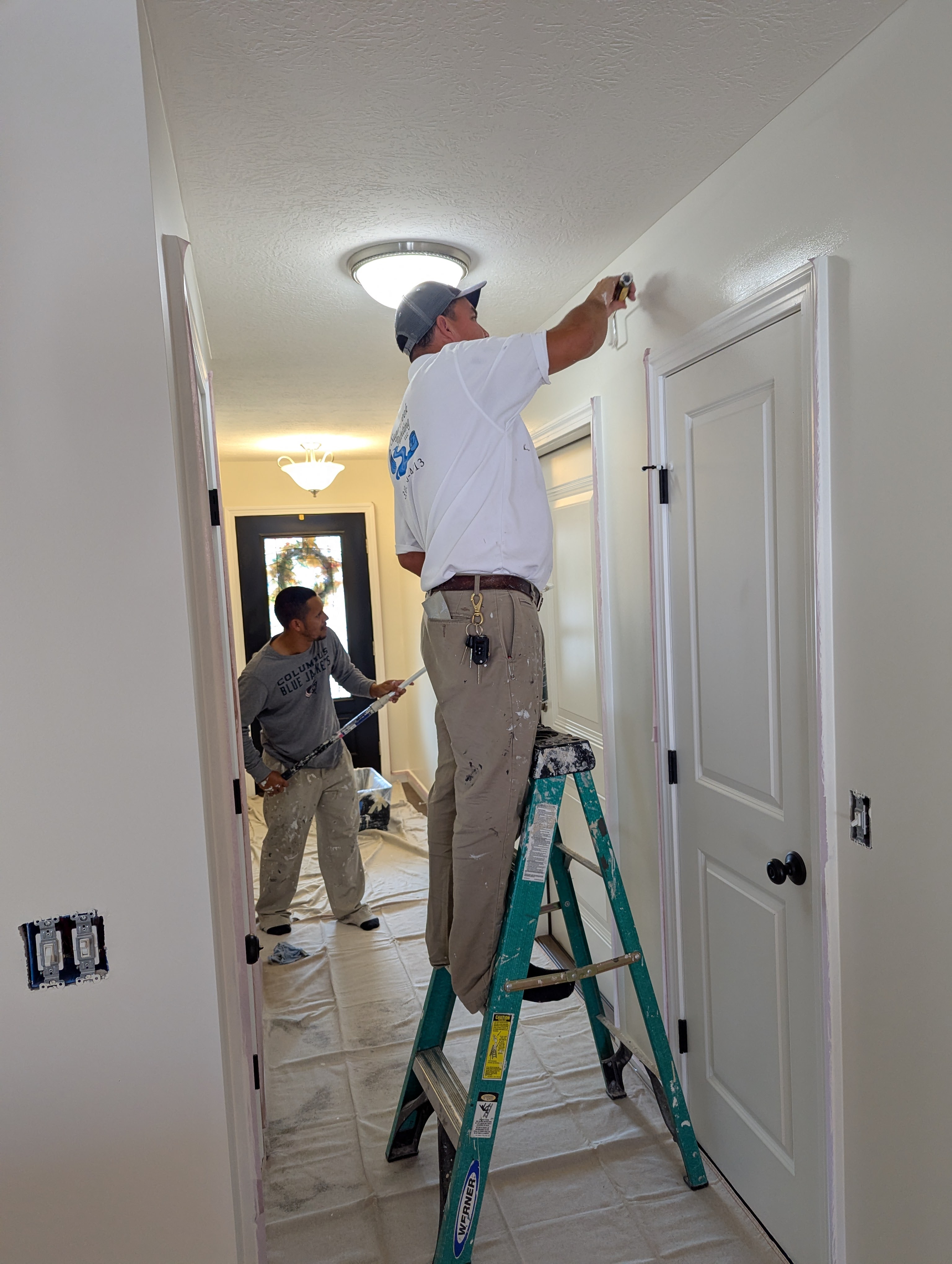 Painters working in a hallway, one on a ladder, painting walls