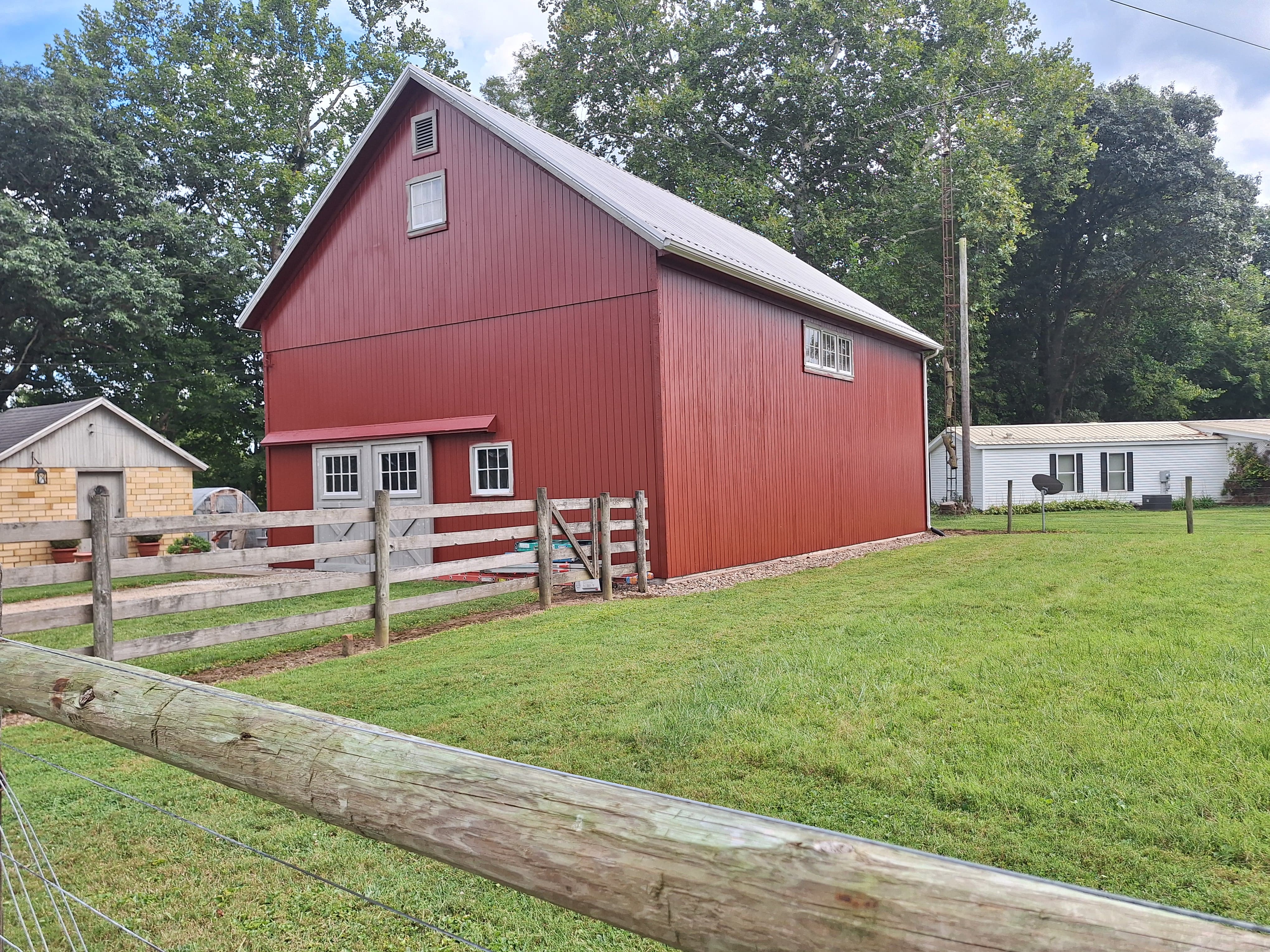 Red barn with white trim, surrounded by a wooden fence and green grass.