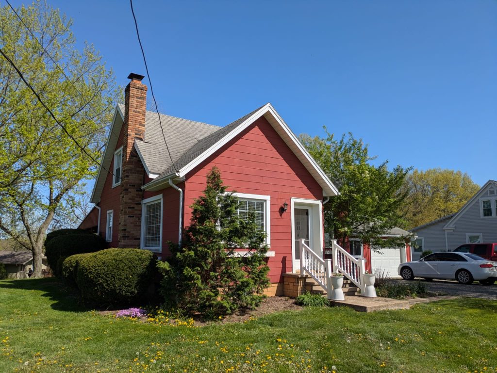 Red Cape Cod Style House Front Yard Red home with white trim, chimney, green lawn, and blue sky.