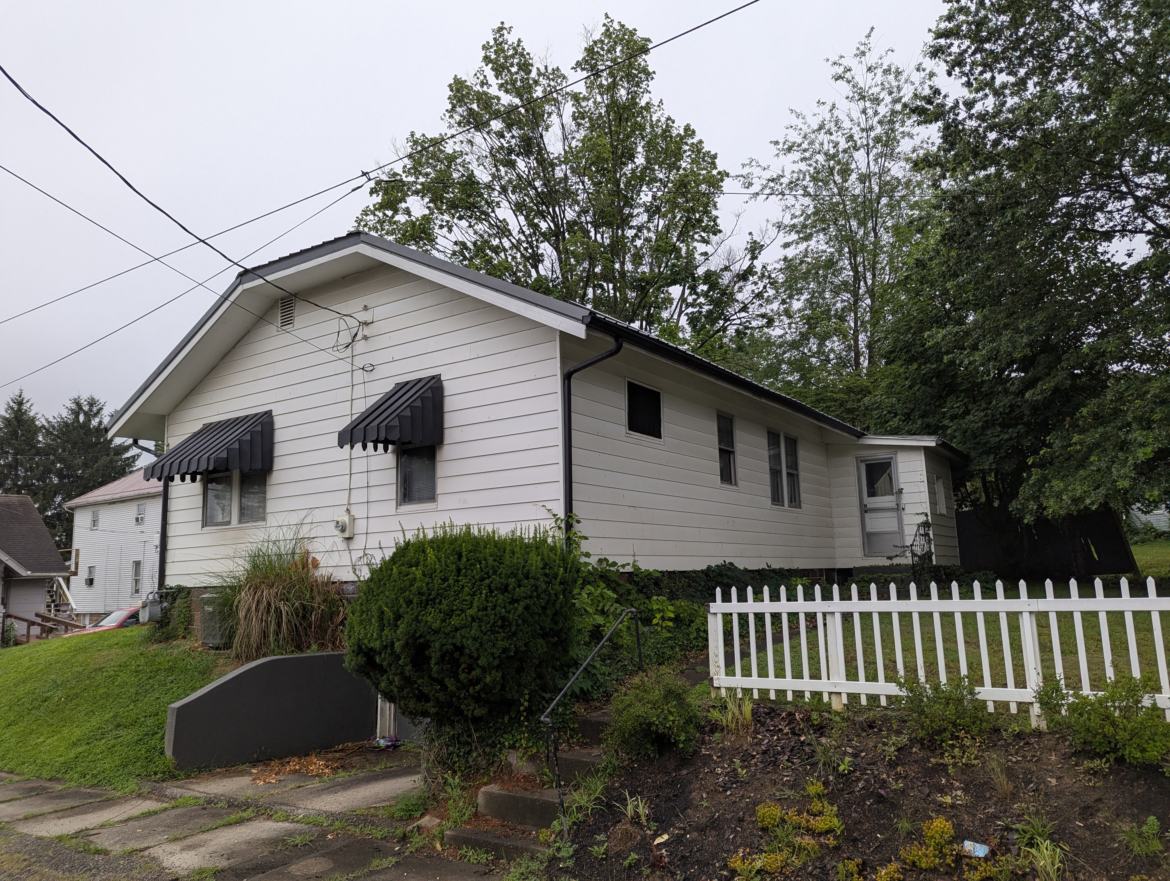 White house with black awnings and a white picket fence.