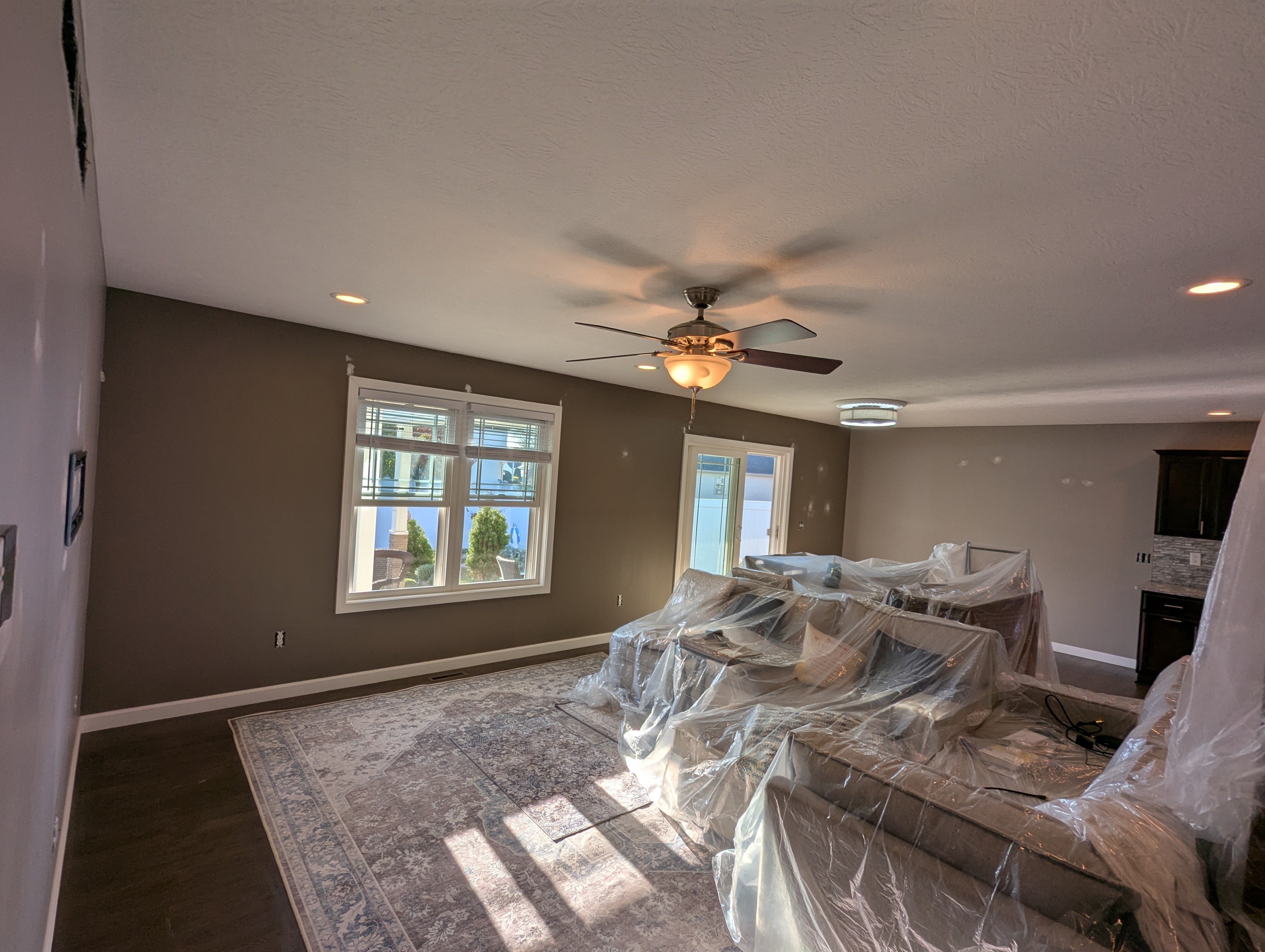 Living room interior with furniture covered in plastic, brown walls, and a ceiling fan.