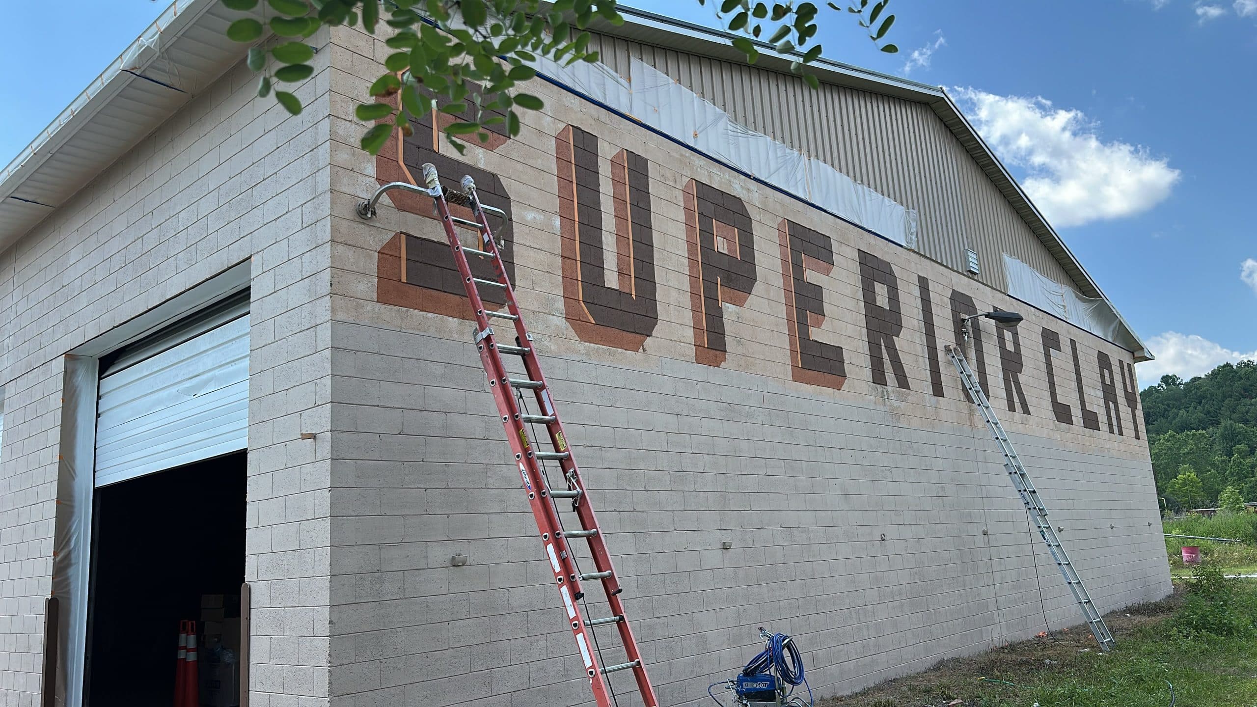 Superior Clean mural being painted on a brick building with ladders and equipment.